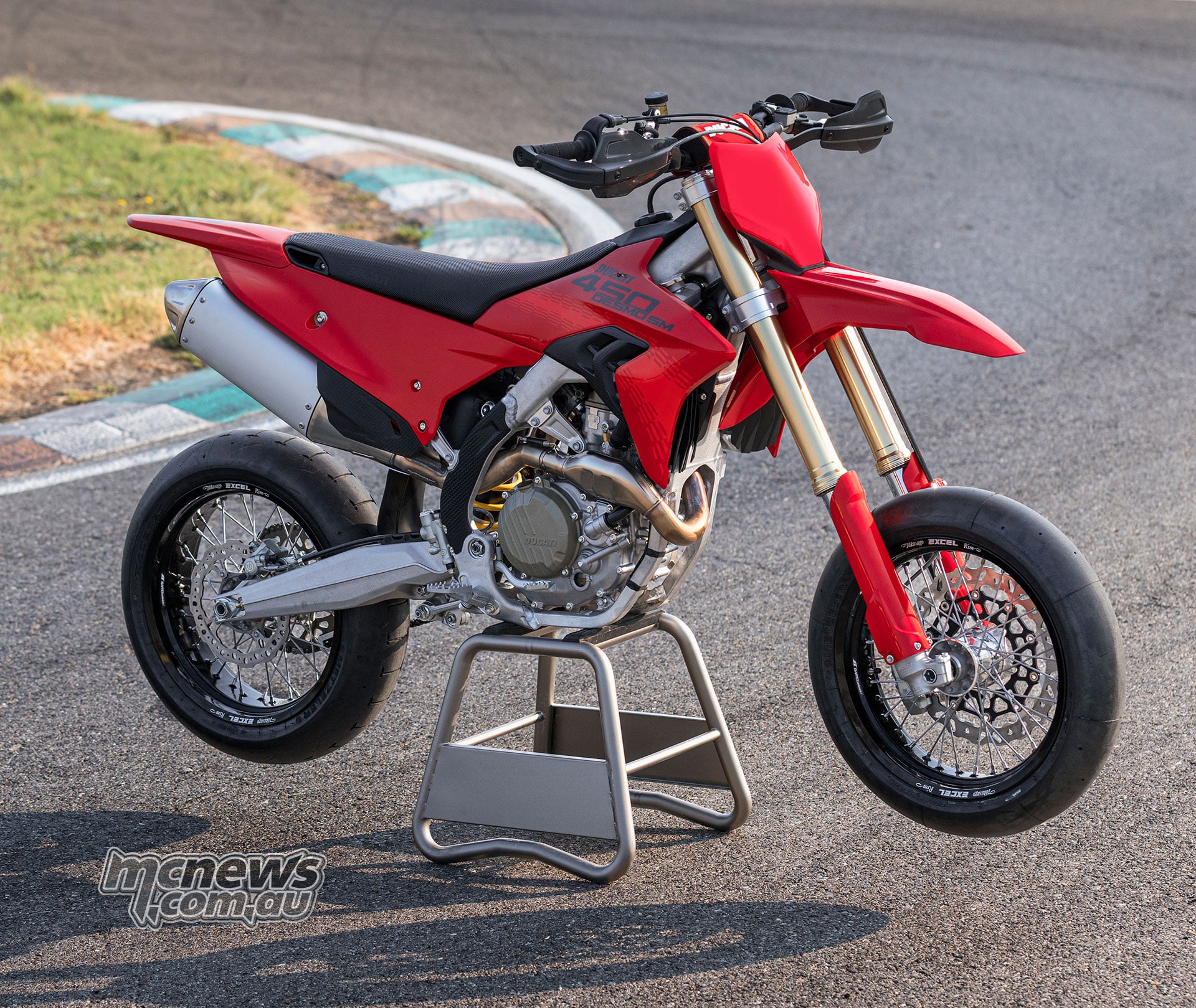 Front three-quarter view of the red Ducati Desmo450 SM on a maintenance stand, showing its slick tyres, gold Showa fork and handguards.