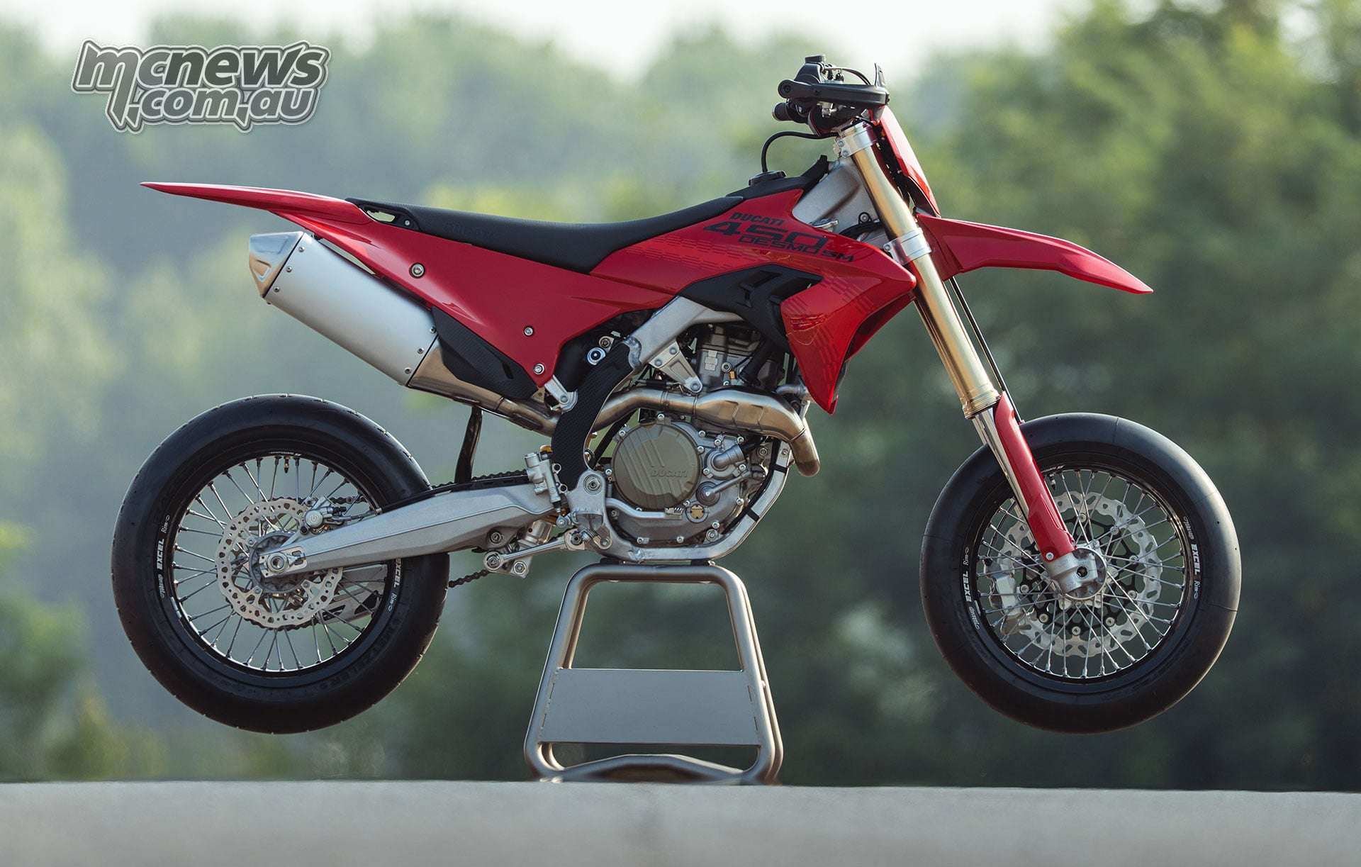Right-side profile of the Ducati Desmo450 SM in Ducati Red on a maintenance stand, showing the engine, exhaust and slick-shod spoked wheels.