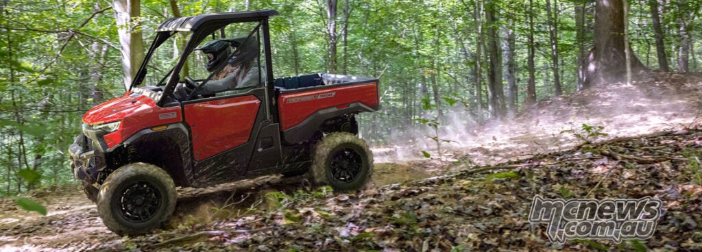 Red Honda Pioneer SXS1000-3 Deluxe driving across a forest trail