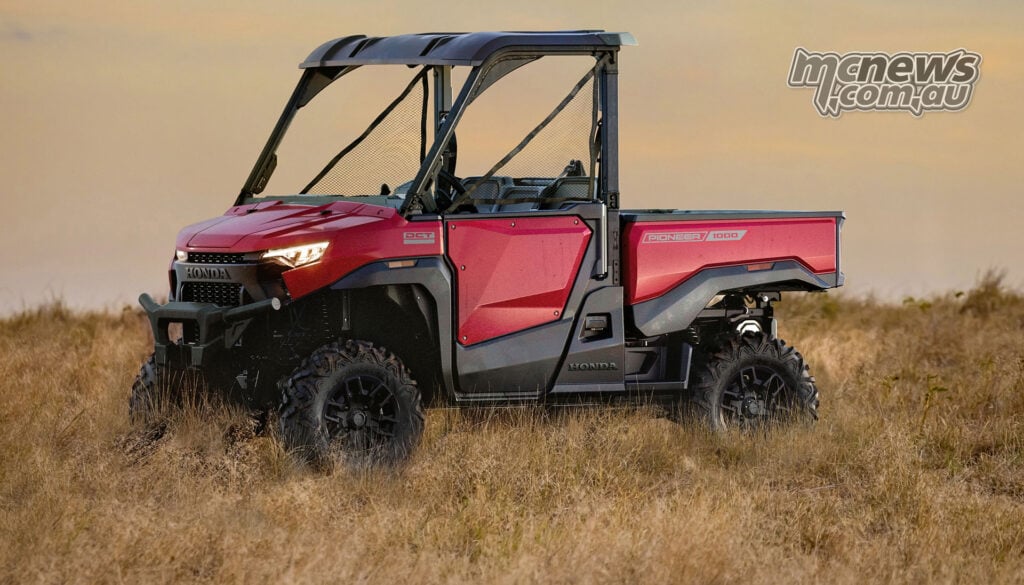 Red Honda Pioneer SXS1000-3 Deluxe parked in dry grass with its LED headlights illuminated