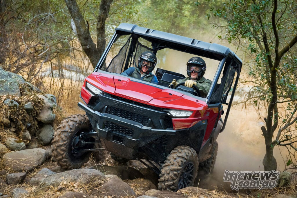 Honda Pioneer SXS1000 Deluxe carrying two helmeted occupants over a rocky trail