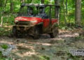 Red 2026 Honda Pioneer SXS1000-5 Deluxe driving through mud on a forest trail