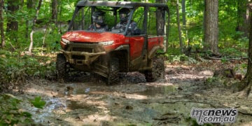 Red 2026 Honda Pioneer SXS1000-5 Deluxe driving through mud on a forest trail