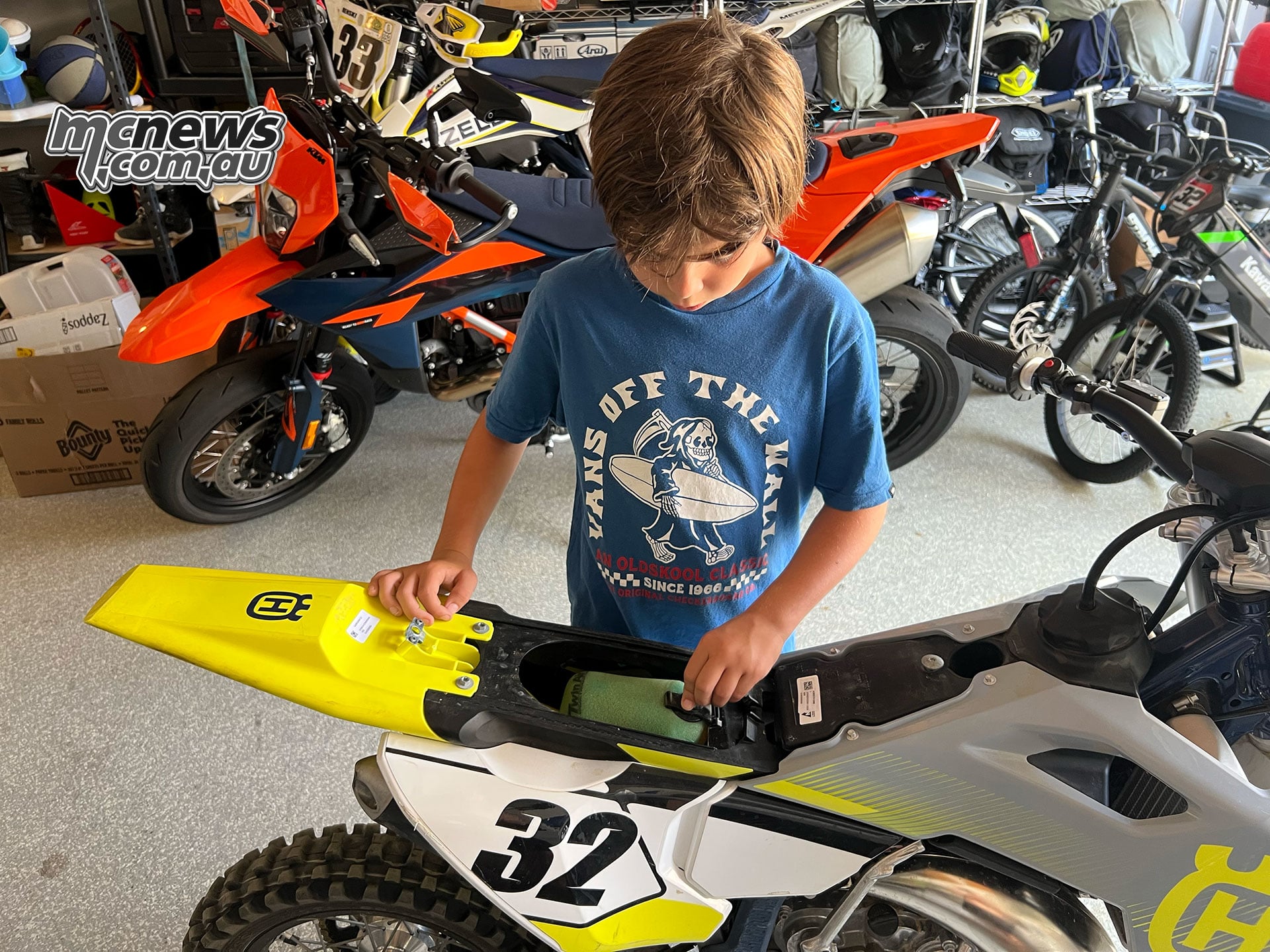 Harvey works at the open airbox of the number 32 Husqvarna TC 65 with the seat removed in the workshop.