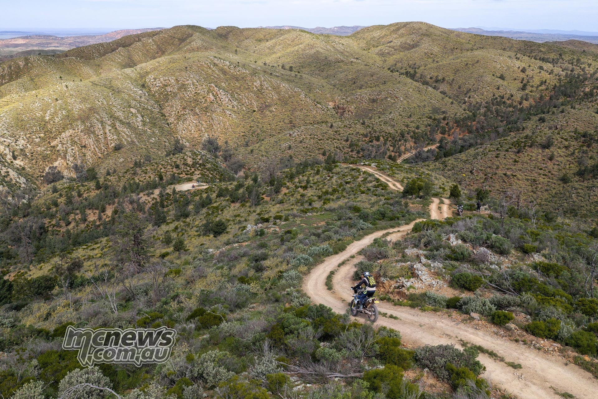 Husqvarna rider follows a winding hillside track above a green valley in the Flinders Ranges.