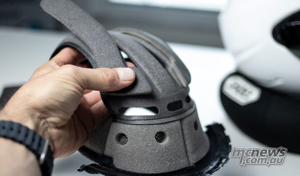 Hand lifting a section of a Shoei centre liner to show PFS adjustment padding underneath.