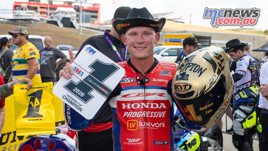 Andrew Lee wears a cowboy hat while holding a Superbike Cup champion number-one plate and gold helmet.