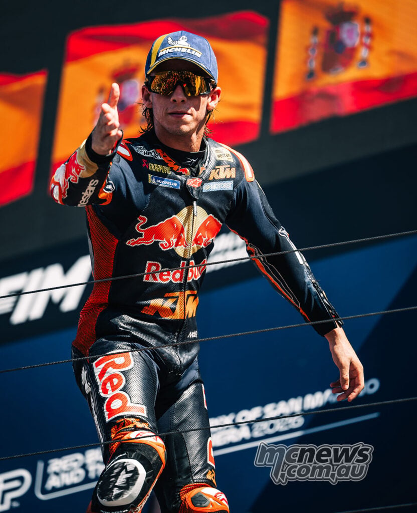 Pedro Acosta gestures towards the crowd while standing on the Misano podium in his KTM leathers.