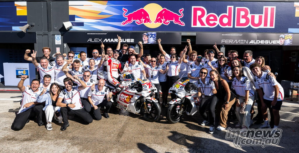 Alex Marquez and Fermin Aldeguer celebrate with the Gresini team and their white-liveried Ducatis outside the garage.