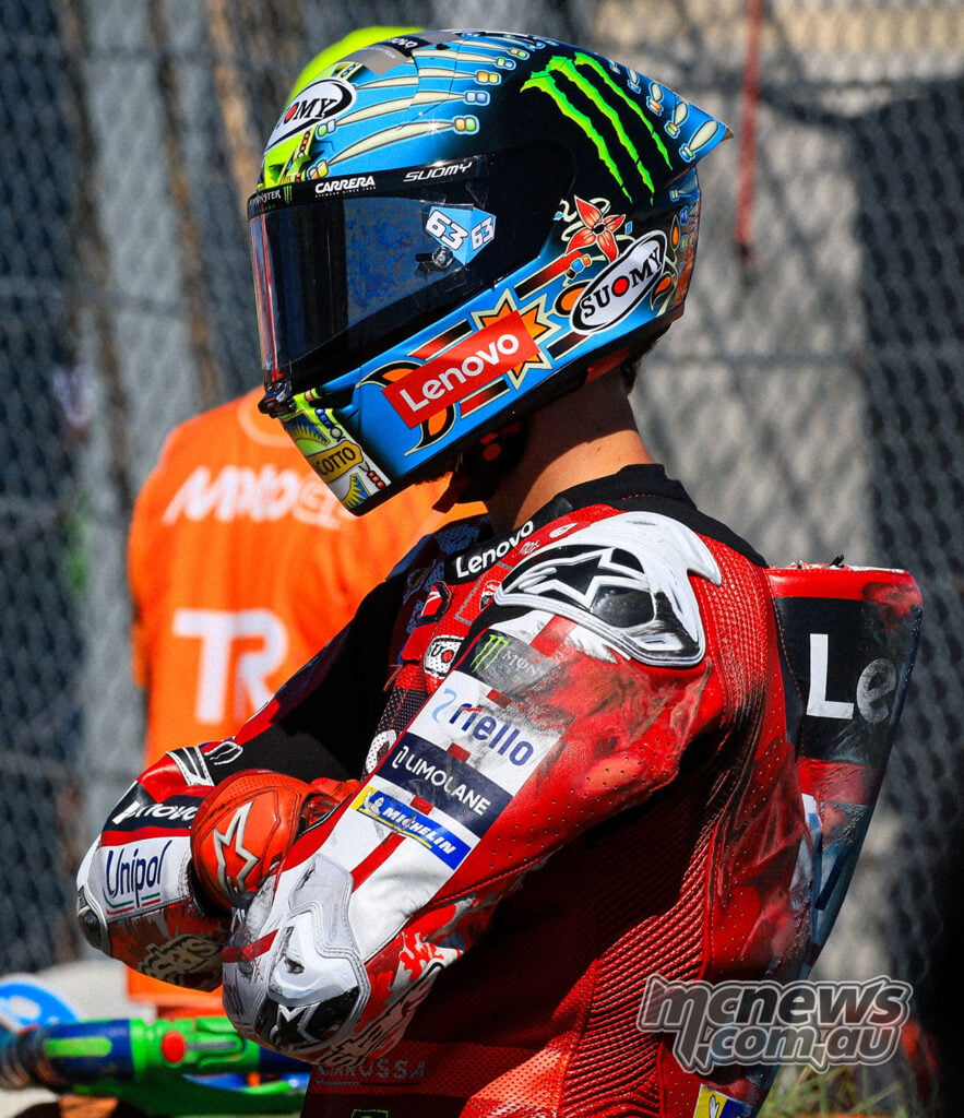 Francesco Bagnaia stands beside the track with his arms folded and blue helmet still on after his crash.