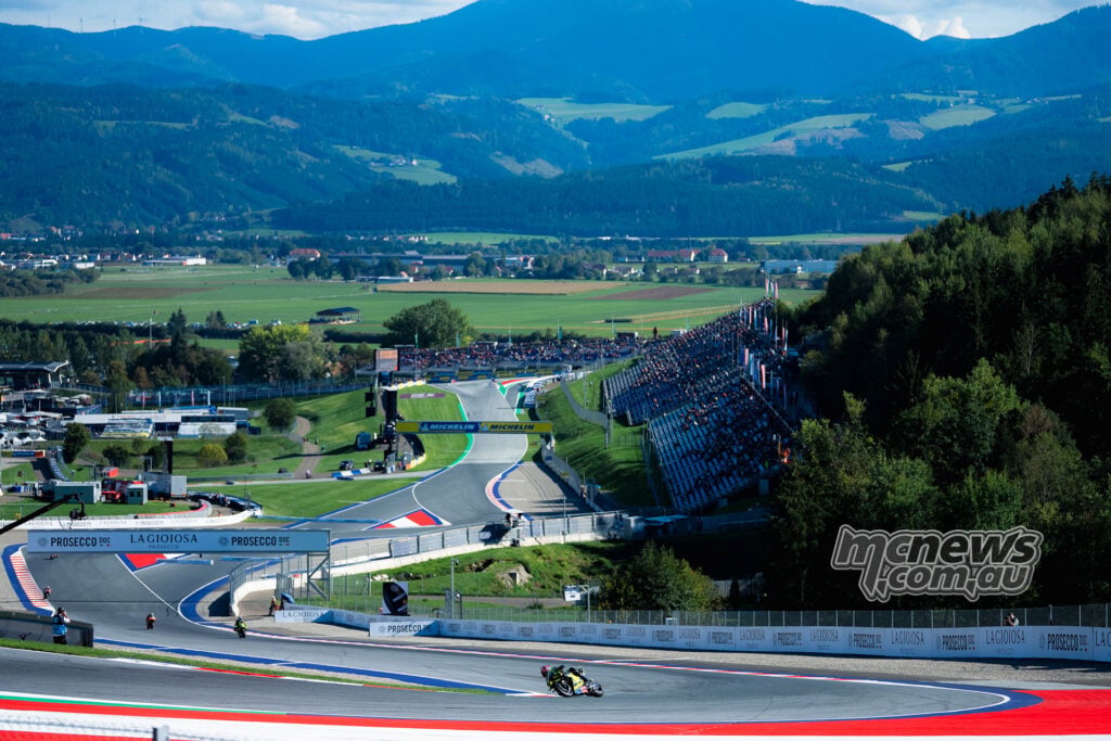 Wide view of Ai Ogura riding through the Red Bull Ring, with grandstands, the valley and surrounding mountains beyond.