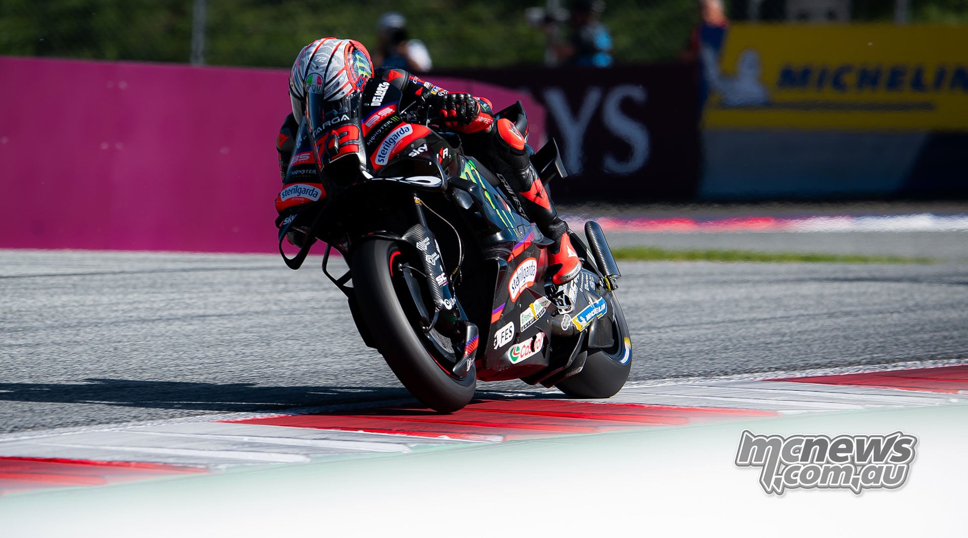Marco Bezzecchi accelerates over the kerbing on his Aprilia with the front wheel raised.