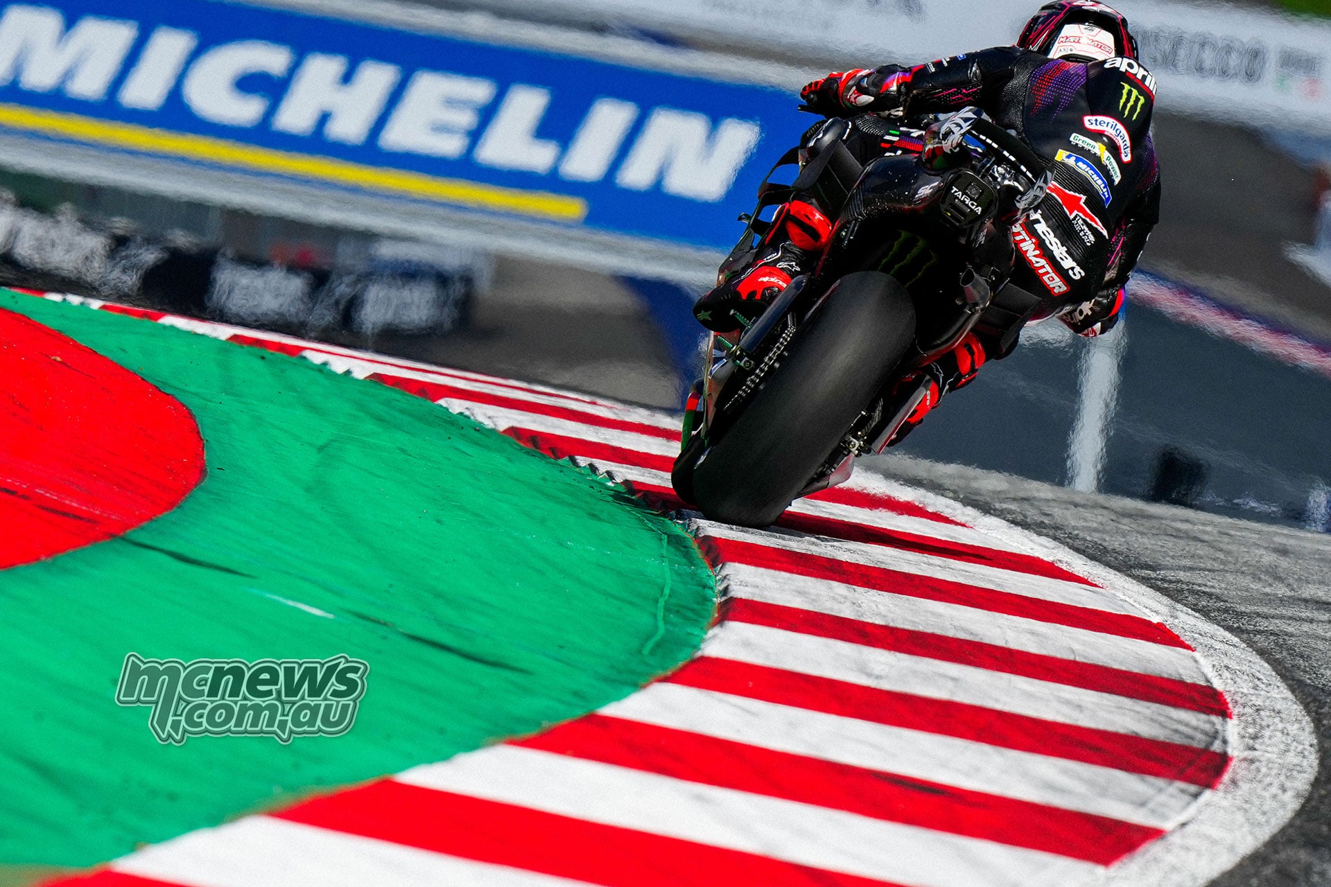 Rear view of Jorge Martin leaning his Aprilia over the red-and-white kerbing in Austria.