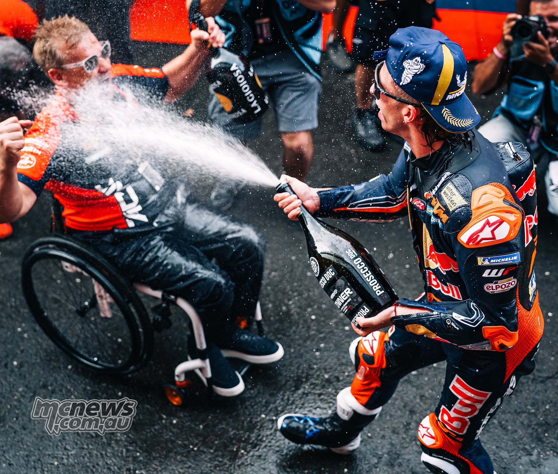Pedro Acosta sprays a celebratory drink towards Pit Beirer, who is seated in his wheelchair.