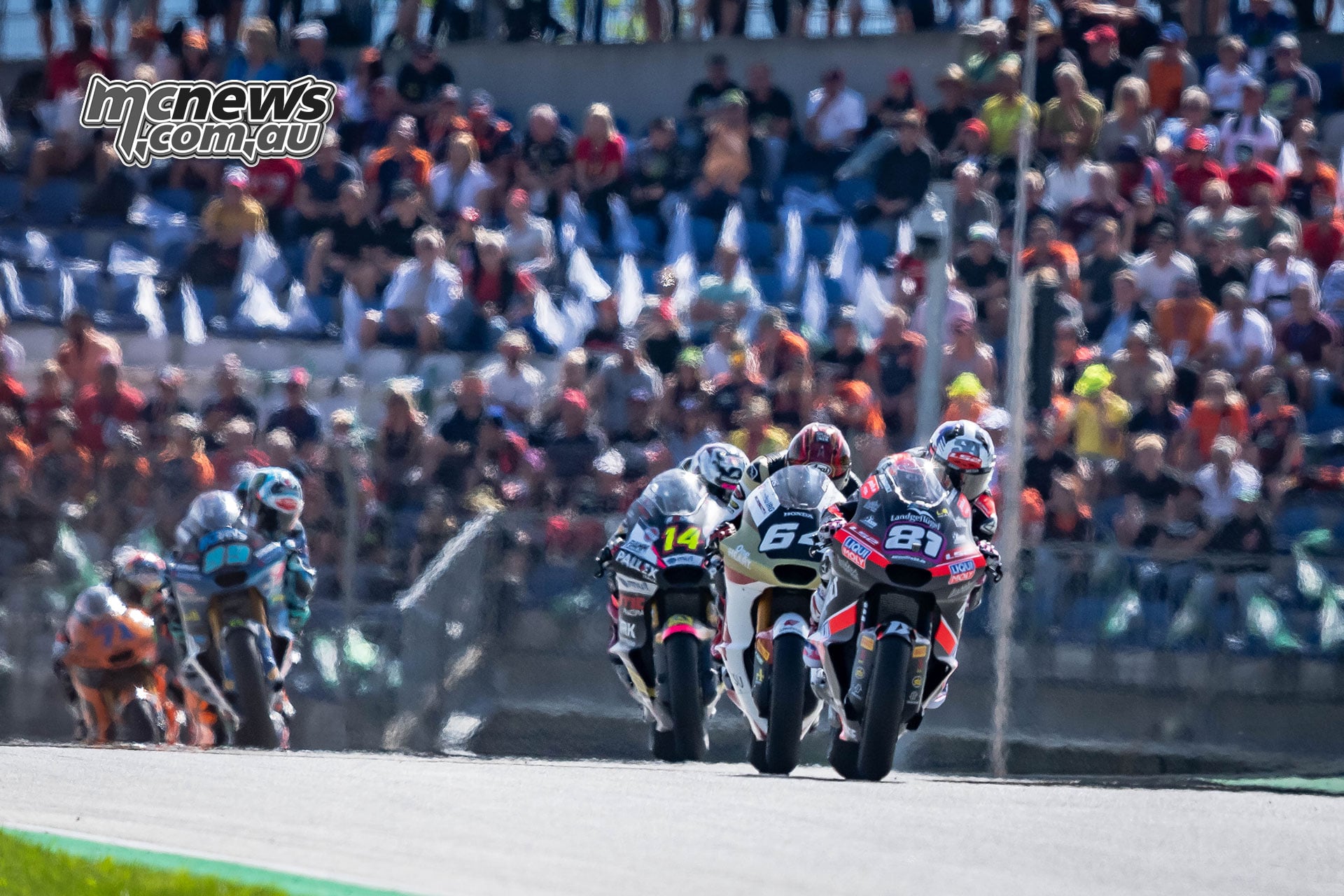 Senna Agius leads a group of Moto2 riders over a rise at the Red Bull Ring, with spectators filling the background.