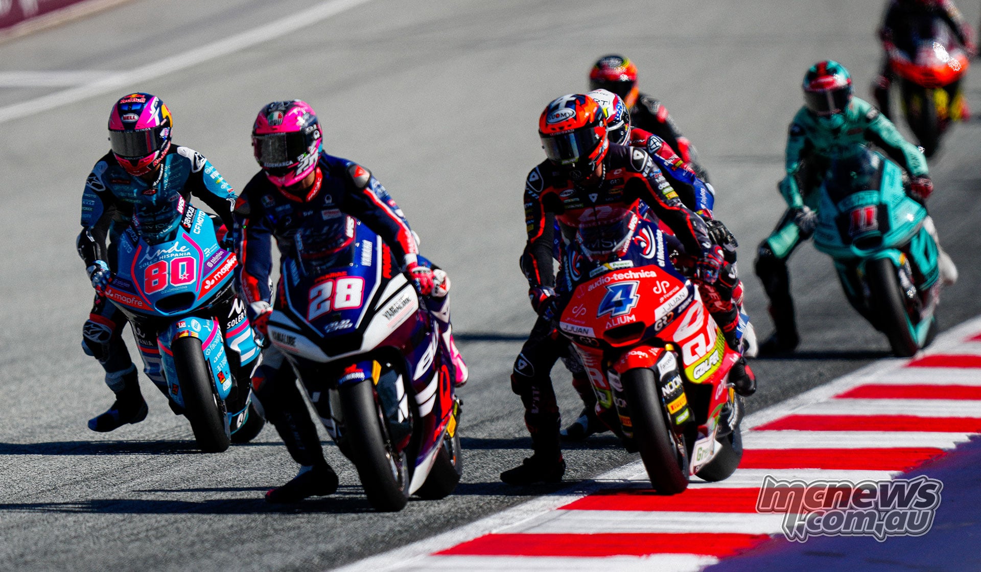 Izan Guevara and Ivan Ortola brake side by side, with David Alonso and other Moto2 riders following.