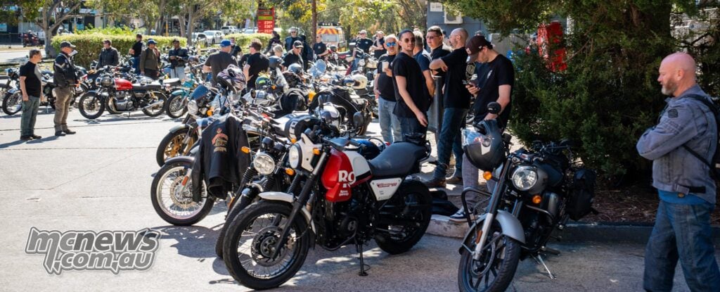 Riders standing beside rows of parked Royal Enfield motorcycles, including a red and white Scram 411, in Sydney.