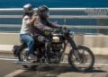 Rider and pillion on a black and cream Royal Enfield crossing a coastal bridge during One Ride 2026.