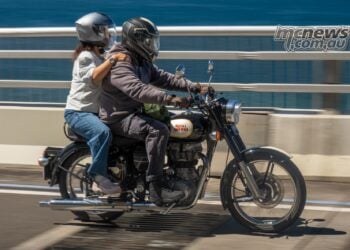 Rider and pillion on a black and cream Royal Enfield crossing a coastal bridge during One Ride 2026.