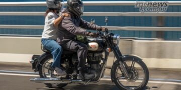 Rider and pillion on a black and cream Royal Enfield crossing a coastal bridge during One Ride 2026.