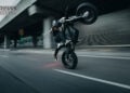 Rider performing a wheelie on a black Stark VARG SM Sköll beneath a concrete overpass.
