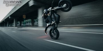 Rider performing a wheelie on a black Stark VARG SM Sköll beneath a concrete overpass.