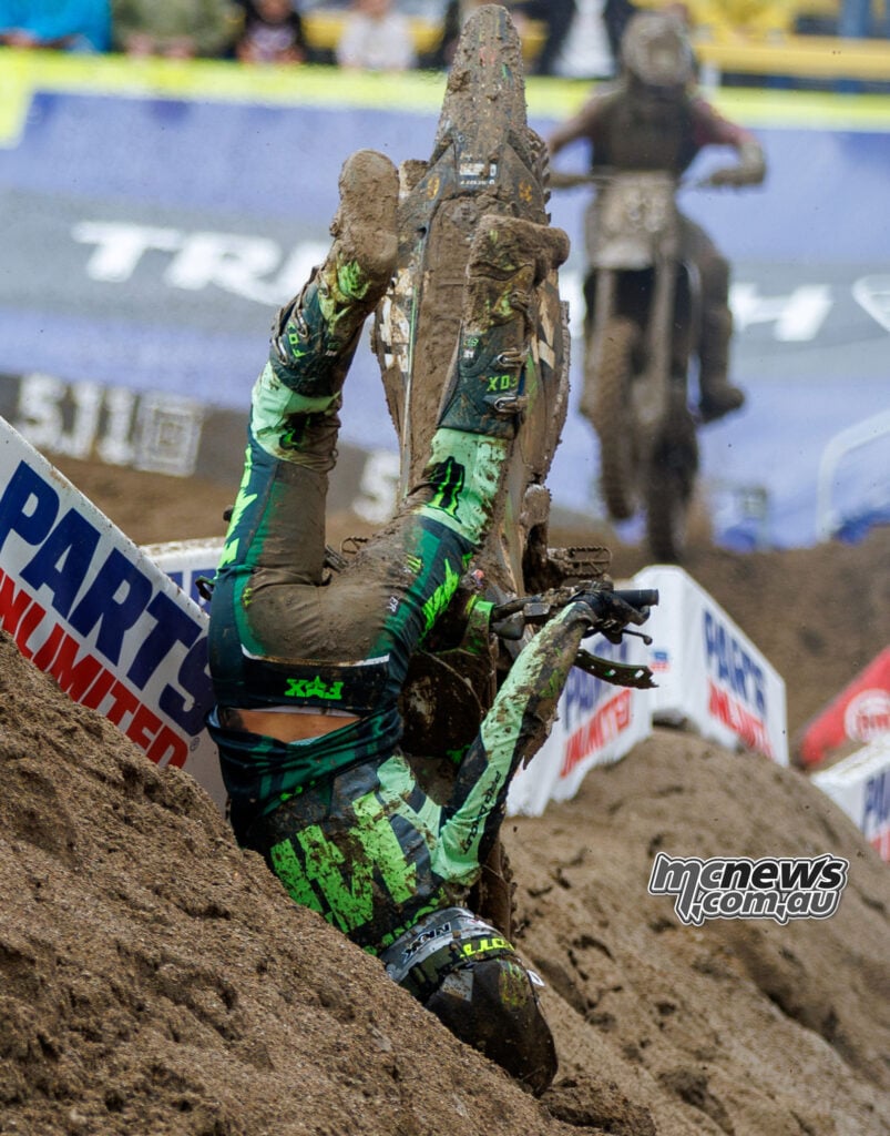 Nicholas Romano tumbles head-first beside a track marker as his mud-covered Kawasaki tips almost vertically above him.