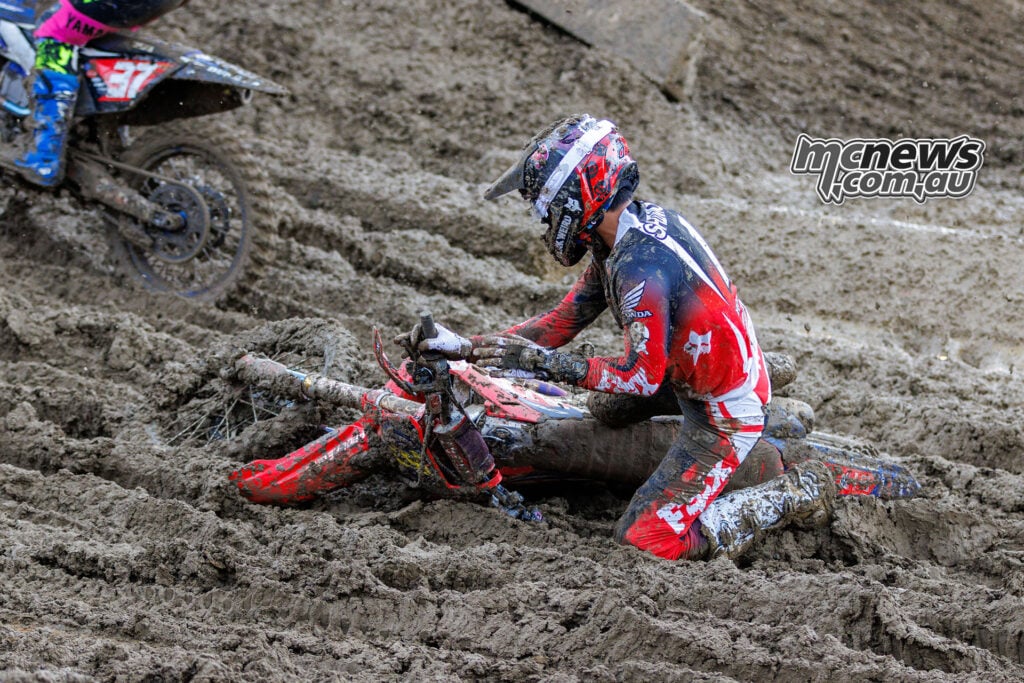 Jo Shimoda kneels beside his fallen Honda in deep mud as Cole Davies' number 37 Yamaha passes at the upper left.