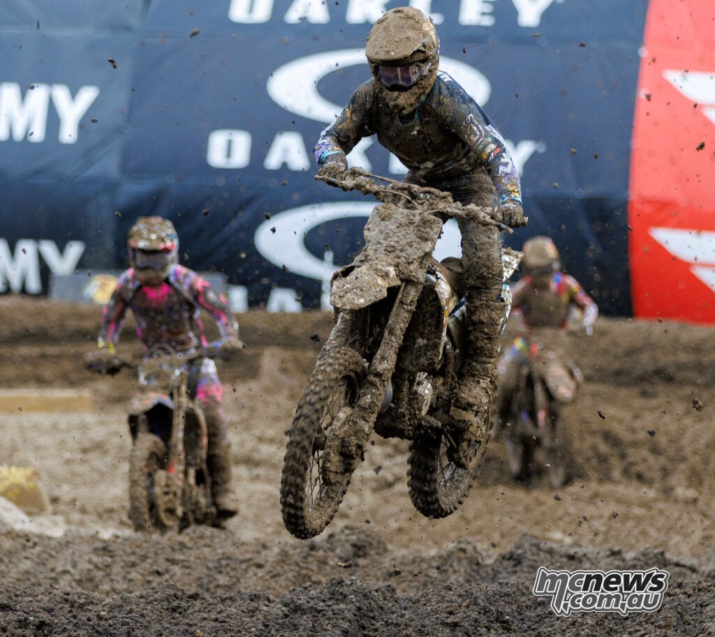 Mud-covered R.J. Hampshire jumps his Husqvarna through the rhythm section with two riders following.