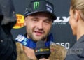 Cooper Webb speaks to a television interviewer with mud on his jersey and goggles around his neck.
