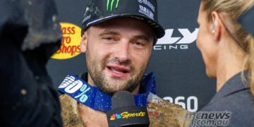 Cooper Webb speaks to a television interviewer with mud on his jersey and goggles around his neck.