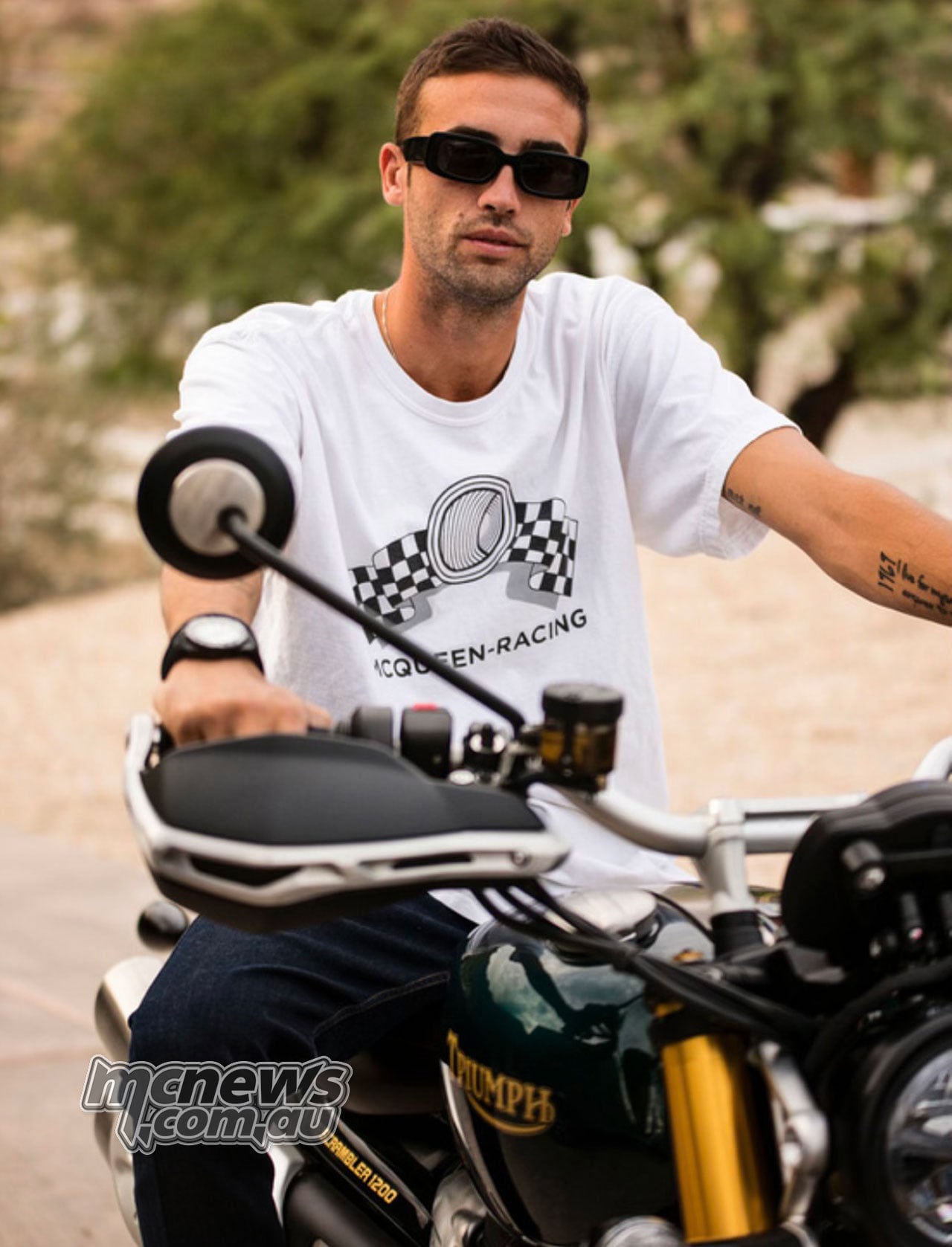 Triumph Originals judge Chase McQueen seated on a green Triumph motorcycle, wearing sunglasses and a white McQueen Racing shirt.