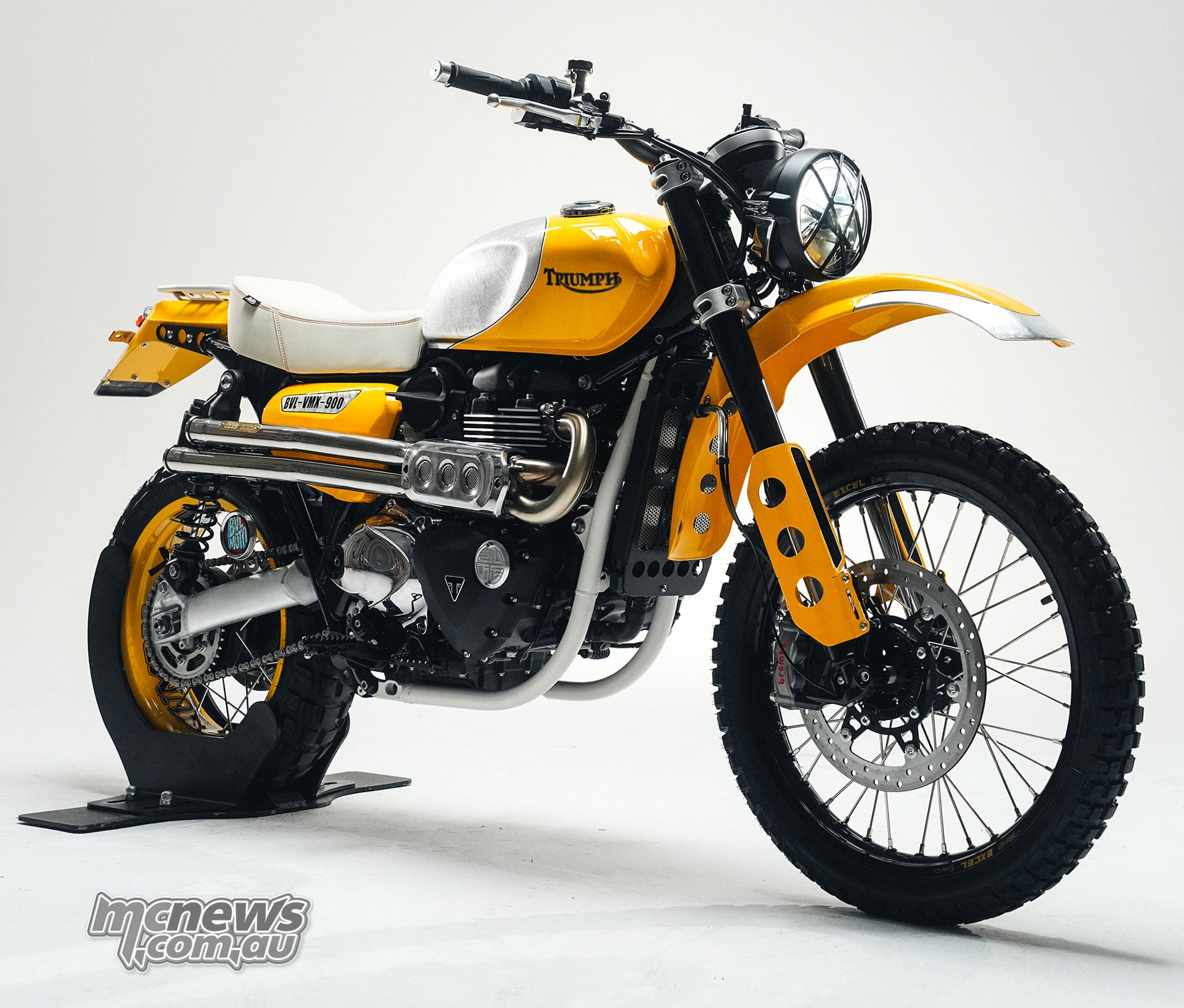 Yellow and white BVL Garage Triumph Scrambler 900 custom with a high front mudguard, spoked wheels and knobby tyres.