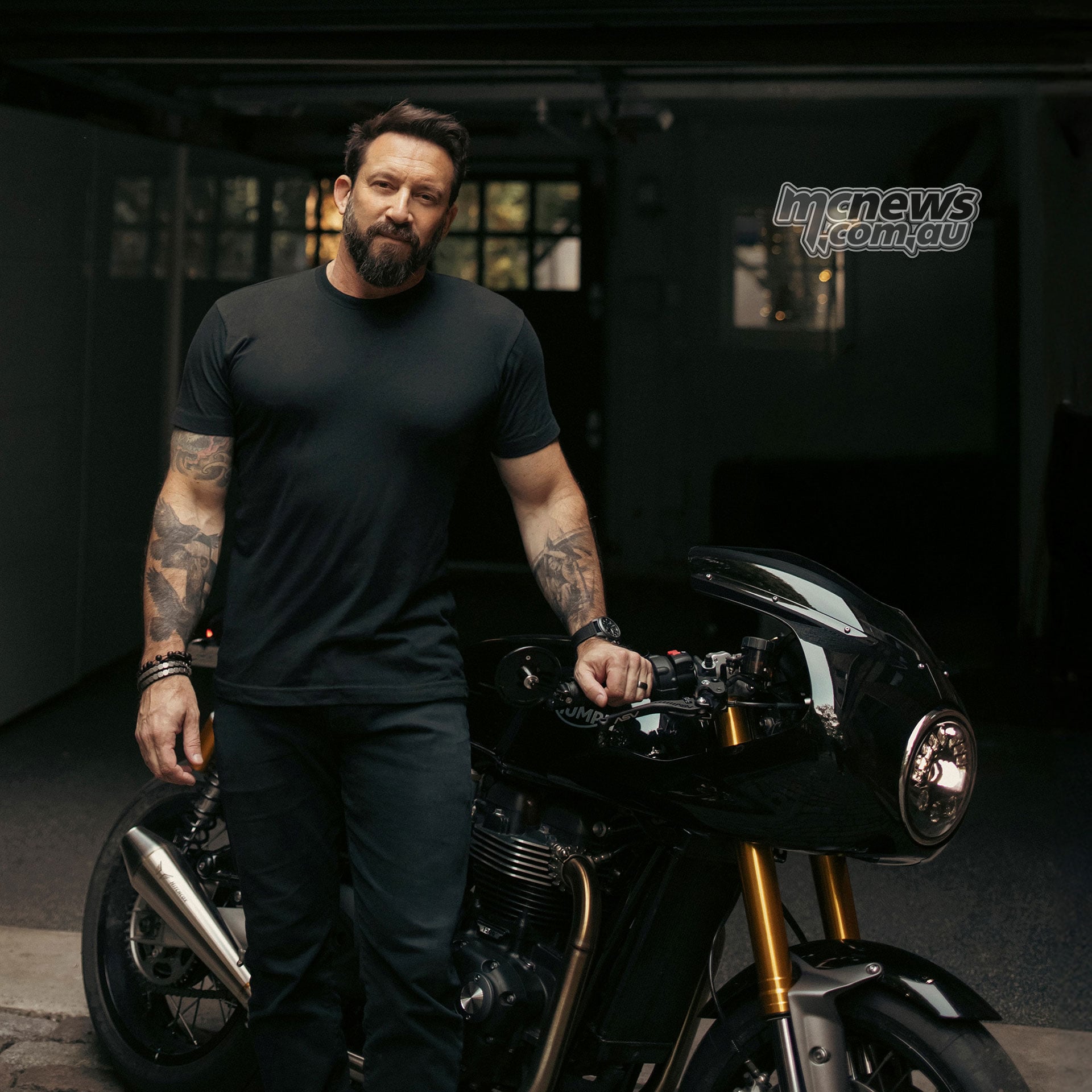 Author and Triumph Originals judge Eric Hendrikx standing beside a black Triumph café racer outside a garage.