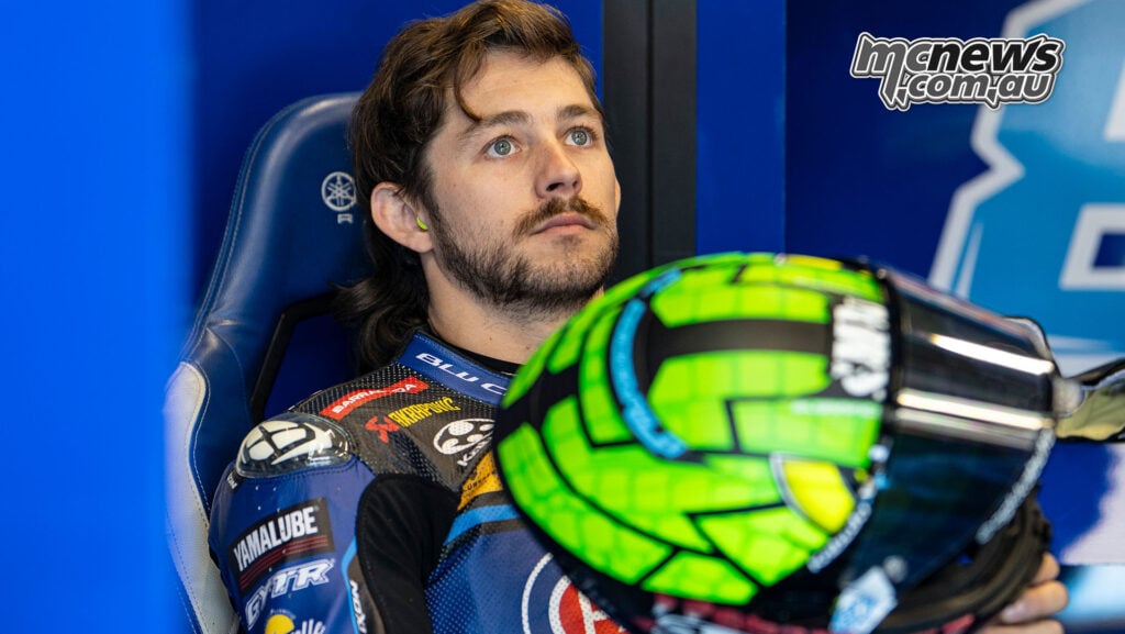 Remy Gardner sits in the Yamaha pit box with his bright green helmet in the foreground.