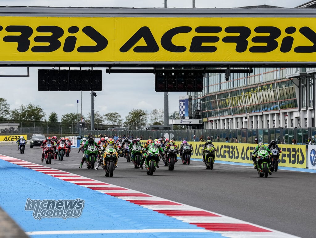 A large field of WorldSPB motorcycles accelerates down the Magny-Cours straight beneath the Acerbis bridge.