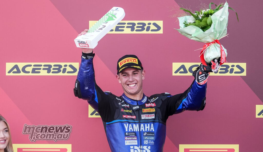 Roberto Garcia smiles on the Magny-Cours podium while holding his second-place trophy and a bouquet of flowers.