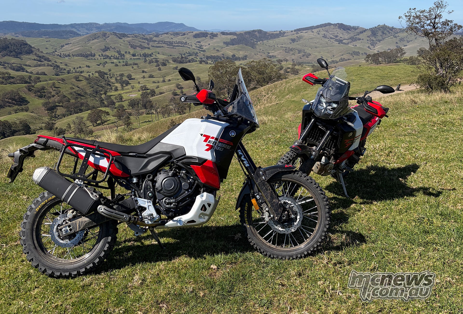 Redline White and Midnight Black Yamaha Ténéré 700 World Raid motorcycles parked on grass above a broad valley.