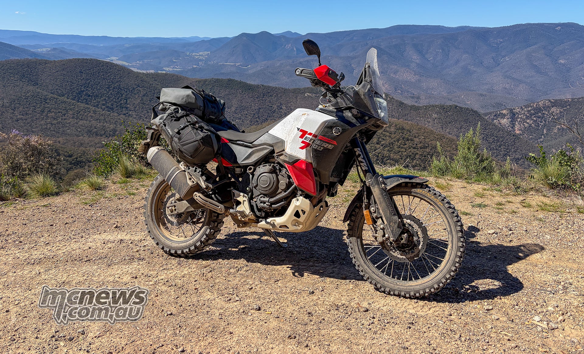 Yamaha Ténéré 700 World Raid with soft luggage parked at a gravel lookout above forested mountain ranges.