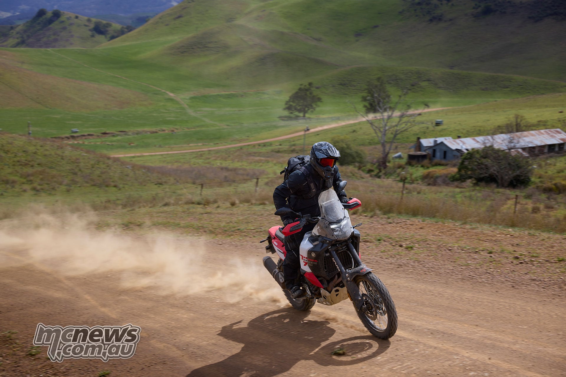 Rider cornering a 2026 Yamaha Ténéré 700 World Raid on dusty gravel with green hills behind.