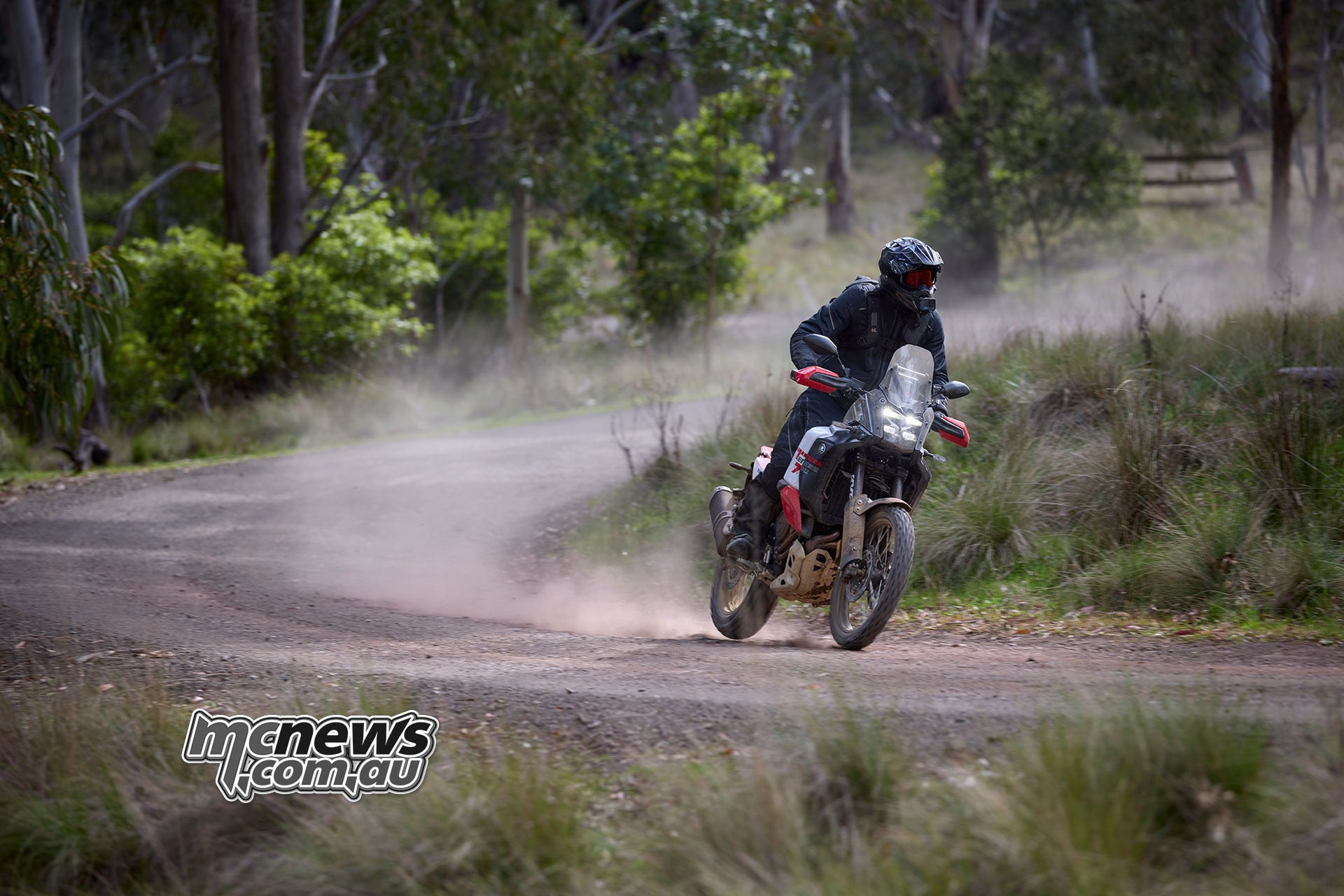 Rider cornering a Yamaha Ténéré 700 World Raid on a winding gravel road with a trail of dust behind.
