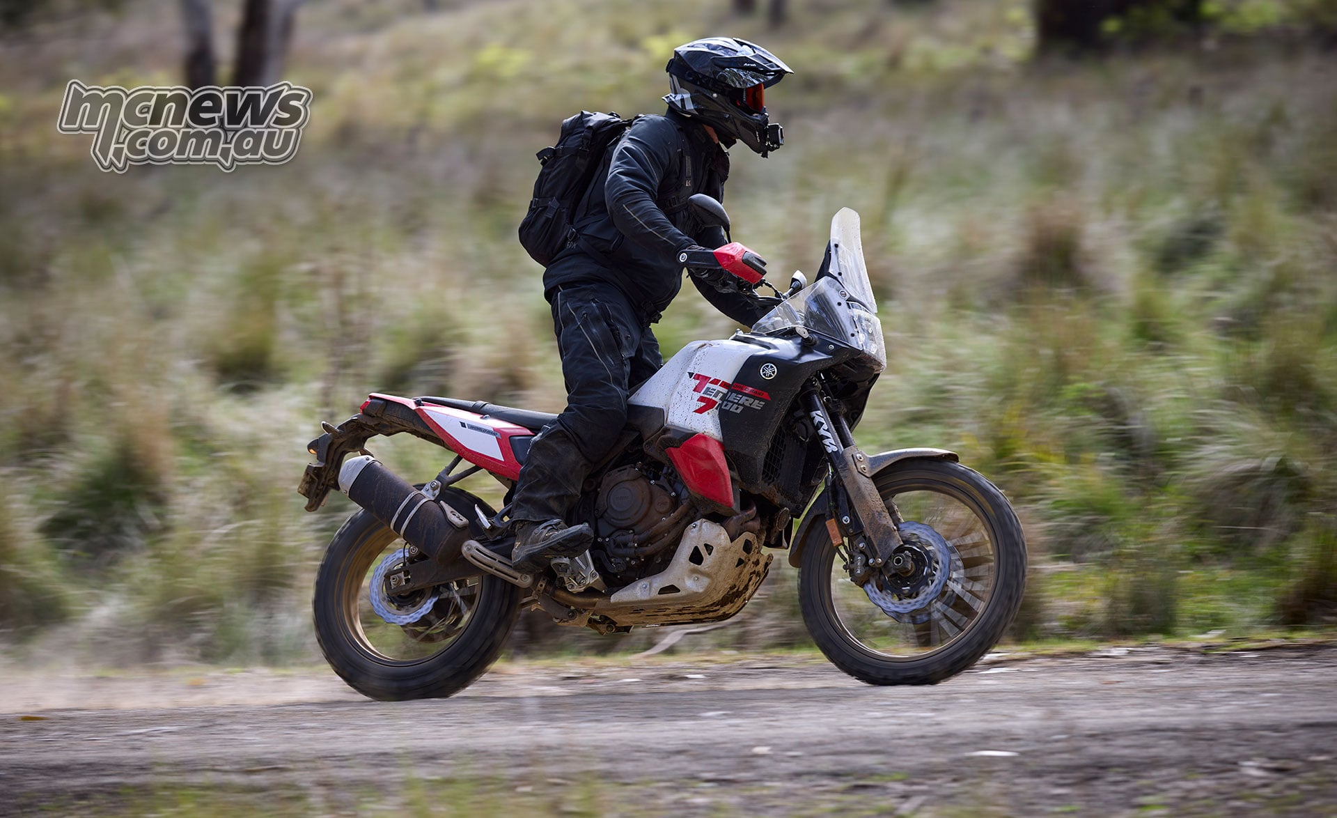 Side view of a rider standing on the pegs of a red and white World Raid while travelling along gravel.