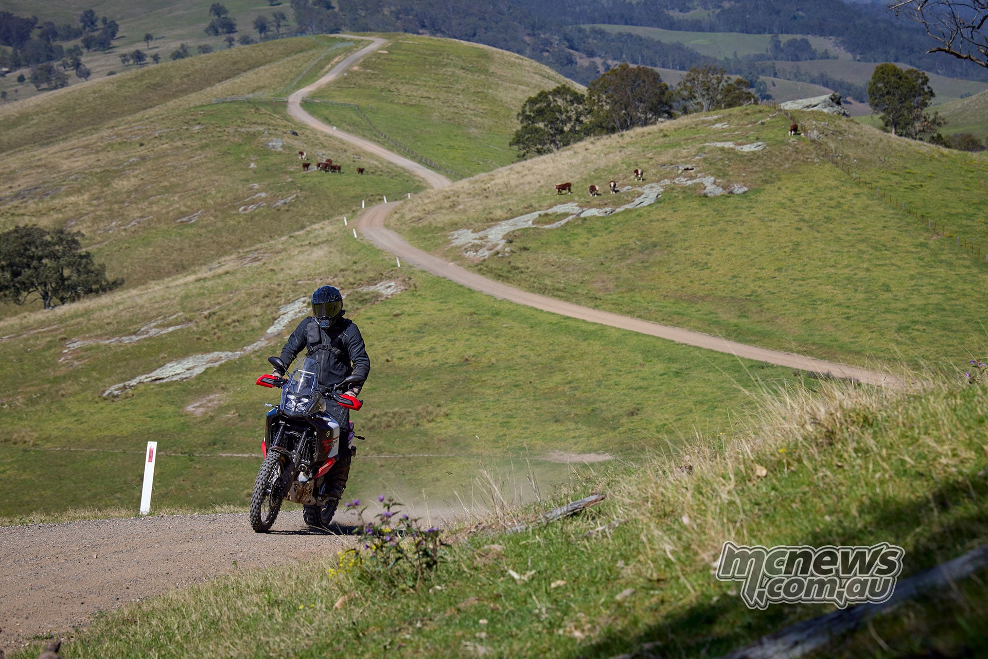 Rider on a Yamaha Ténéré 700 World Raid following a gravel road through rolling green hills.