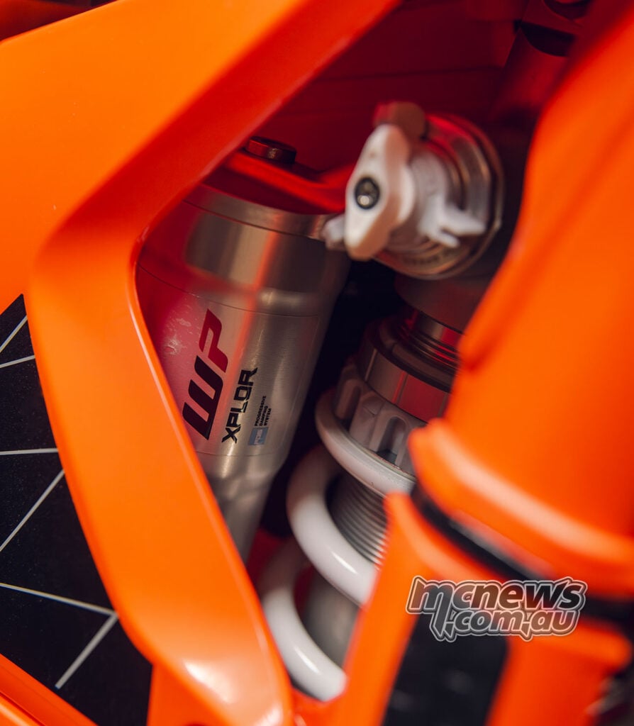 Close-up of the WP XPLOR rear shock reservoir and spring inside the orange KTM frame.