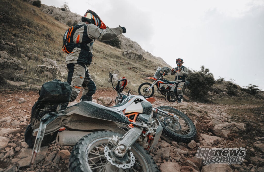 KTM 690 Rally motorcycles and riders stopped on a steep rocky off-road trail