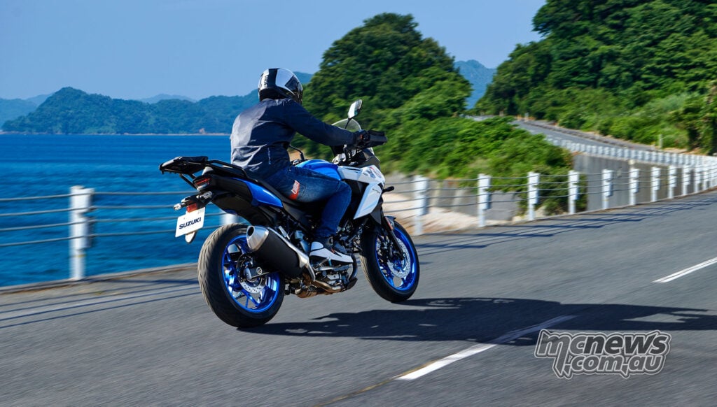 Rear three-quarter view of a blue and white Suzuki SV-7GX riding along a coastal road
