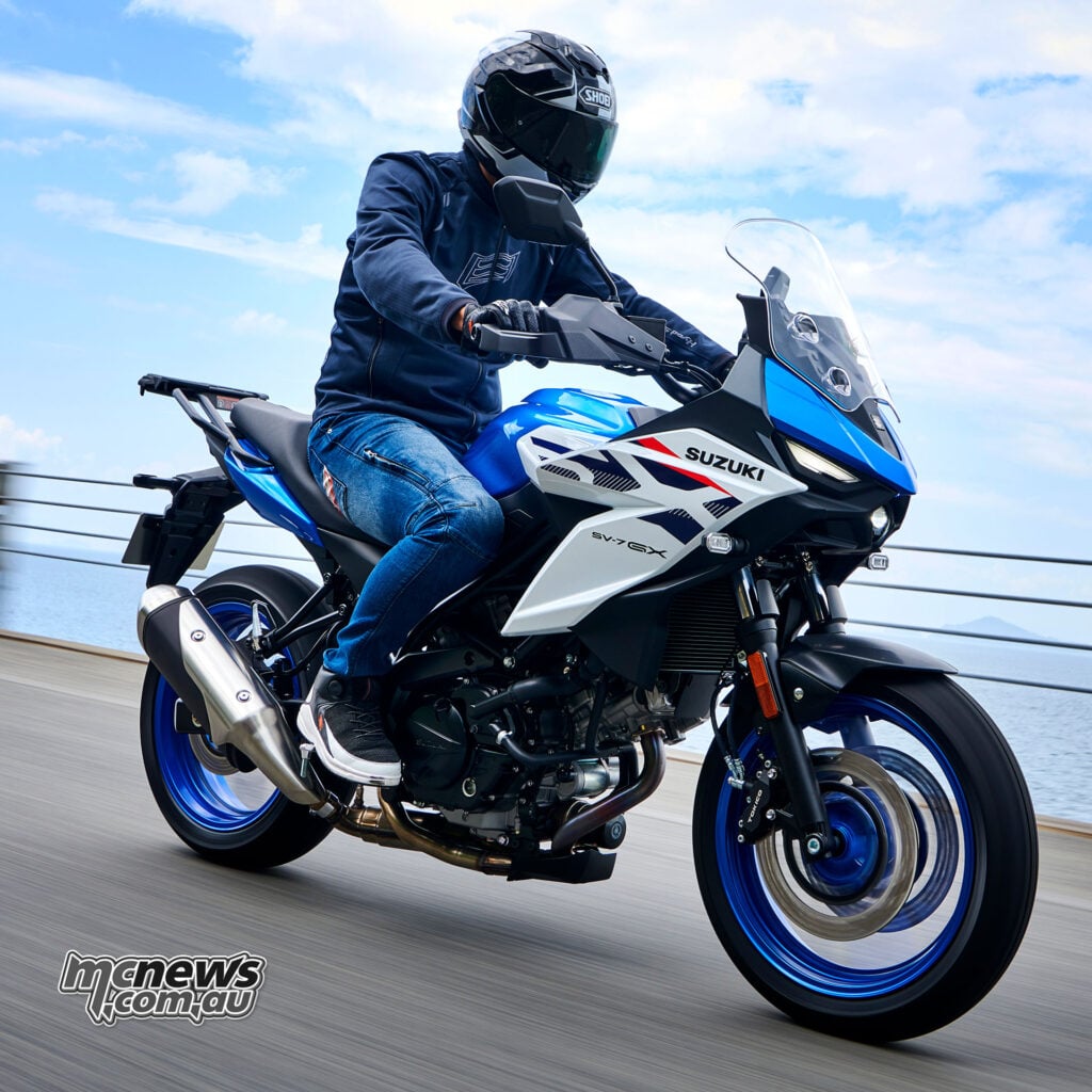Low front three-quarter action view of a rider on a blue and white 2027 Suzuki SV-7GX