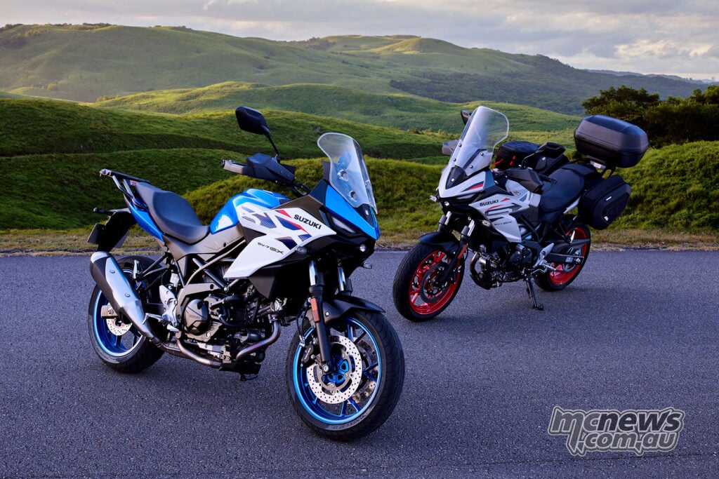 Blue and white standard Suzuki SV-7GX parked beside a Pearl Matte Greige SV-7GX fitted with touring luggage in green hills