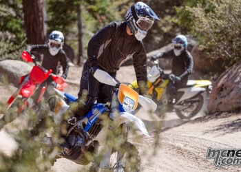 Three enduro riders wearing Cardo Venture helmets ride dirt bikes through a rocky forest trail.