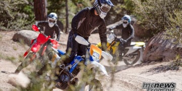 Three enduro riders wearing Cardo Venture helmets ride dirt bikes through a rocky forest trail.